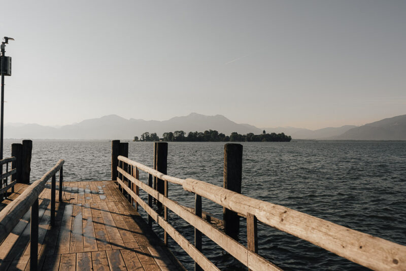 Steg in Gstadt: Fraueninsel mit den Alpen im Hintergrund.