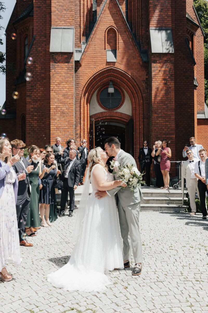 Brautpaar küsst sich im Spalier vor der Erlöserkirche Rosenheim