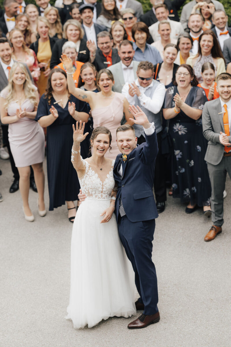 Brautpaar fröhlich beim Gruppenbild mit den Hochzeitsgästen