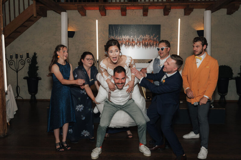 Spaßiges Gruppenbild mit Brautpaar und Hochzeitsgästen während der Feier an der Mühle in Holzham