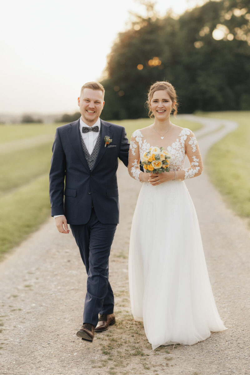 Brautpaar geht auf einem Weg beim Brautpaarshooting zum Sonnenuntergang