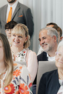 Gäste strahlen zum Brautpaar während der Trauung